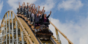 riders of a wooden roller coaster with their hands up